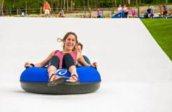 Visitors riding inflatable tubes down a summer outdoor slope