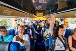 Cheerful group of travelers riding together on a tour bus, smiling and raising their hands in excitement�perfectly capturing the ease and fun of organized travel through Branson Group Tours.